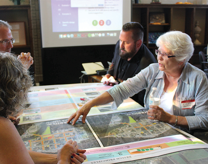 An older woman speaks with other adults while gesturing to a map