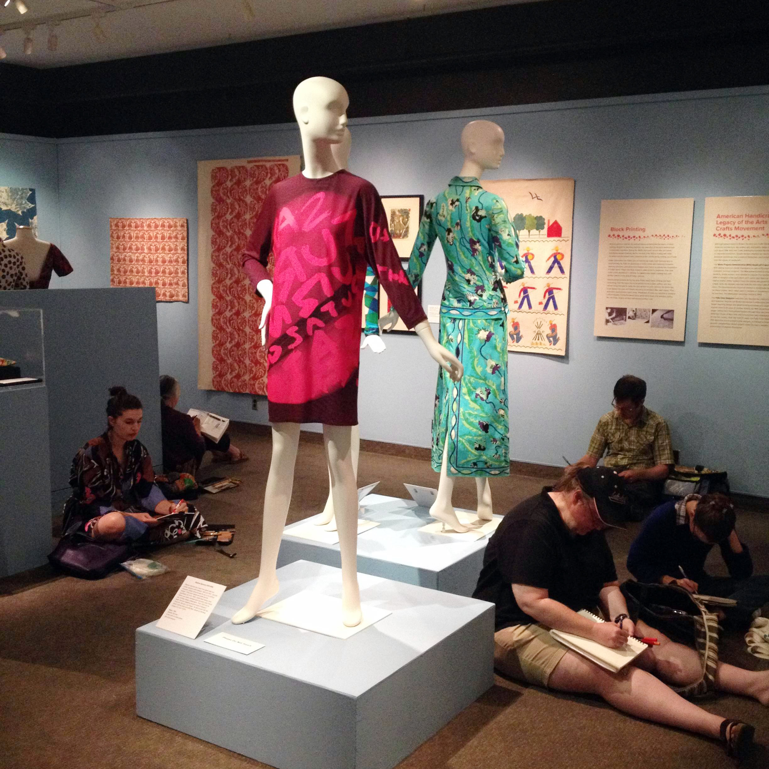 Printed Textiles Pattern Stories exhibition with patterns on display on the wall and on mannequins and students taking notes