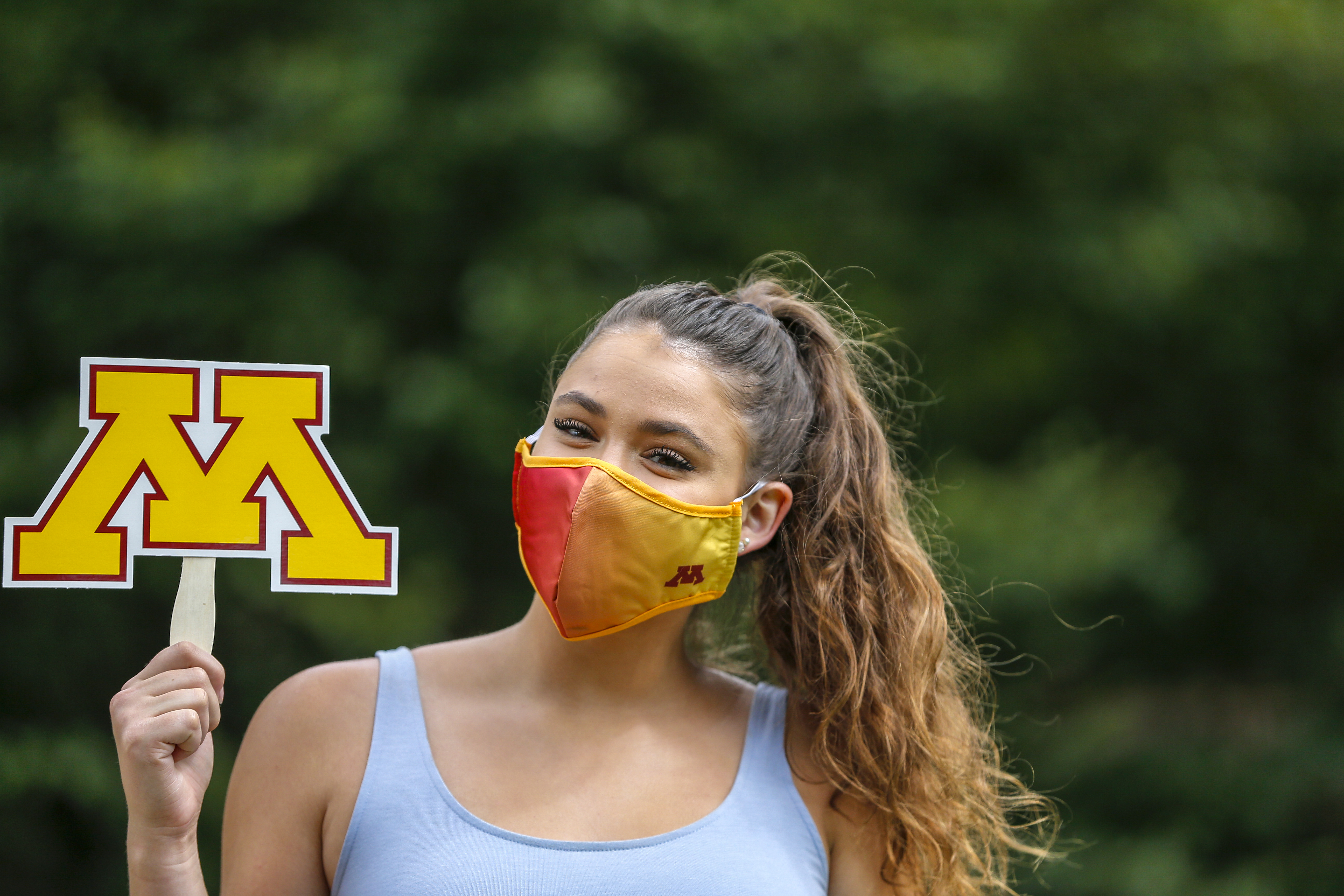 Student wearing a face mask holding the UMN logo