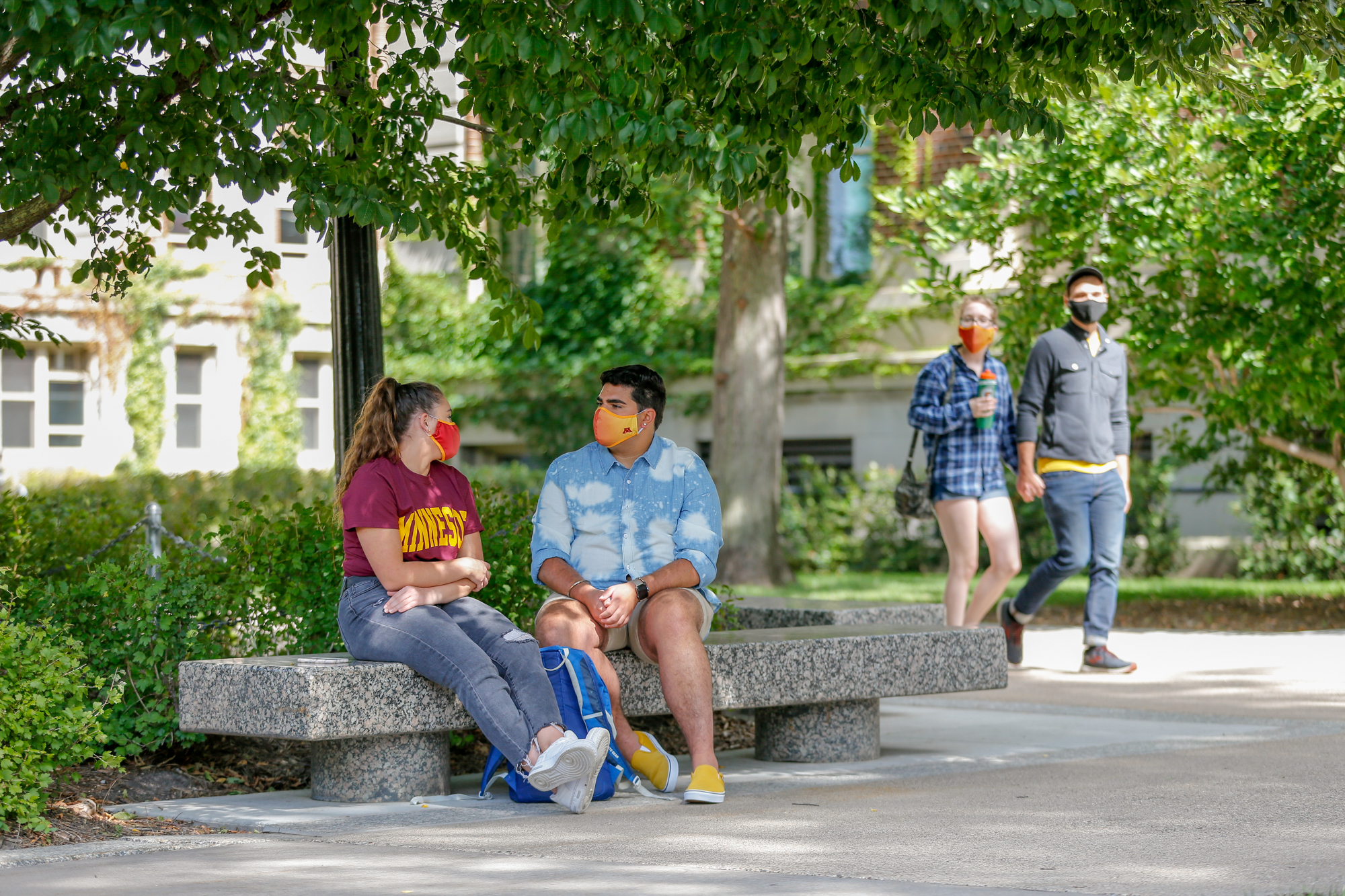 Masked students chatting on a bench on campus. 