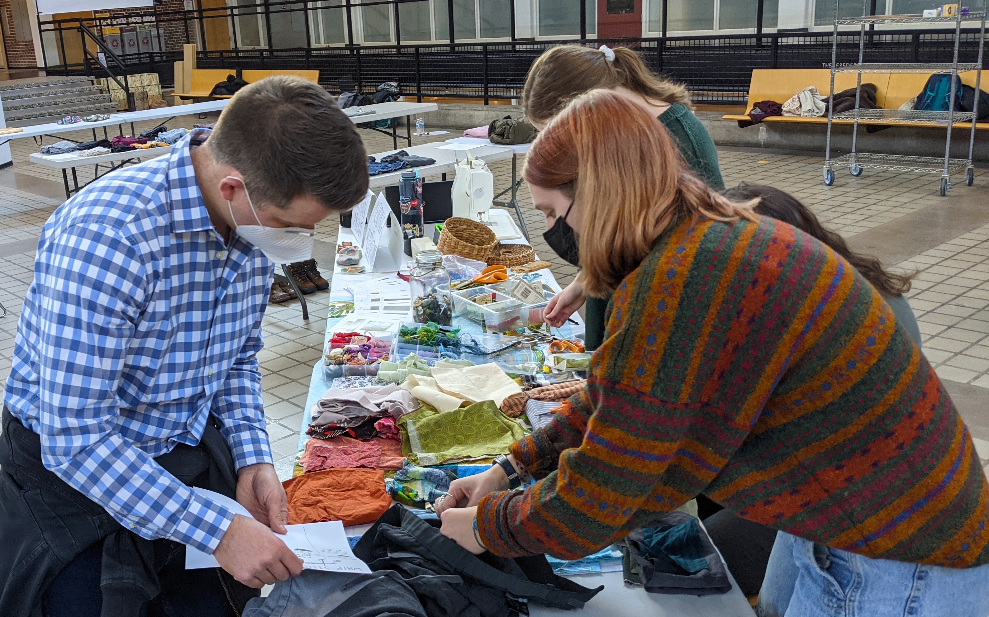 Students help someone repair an item of clothing at the Dare to Repair Fair