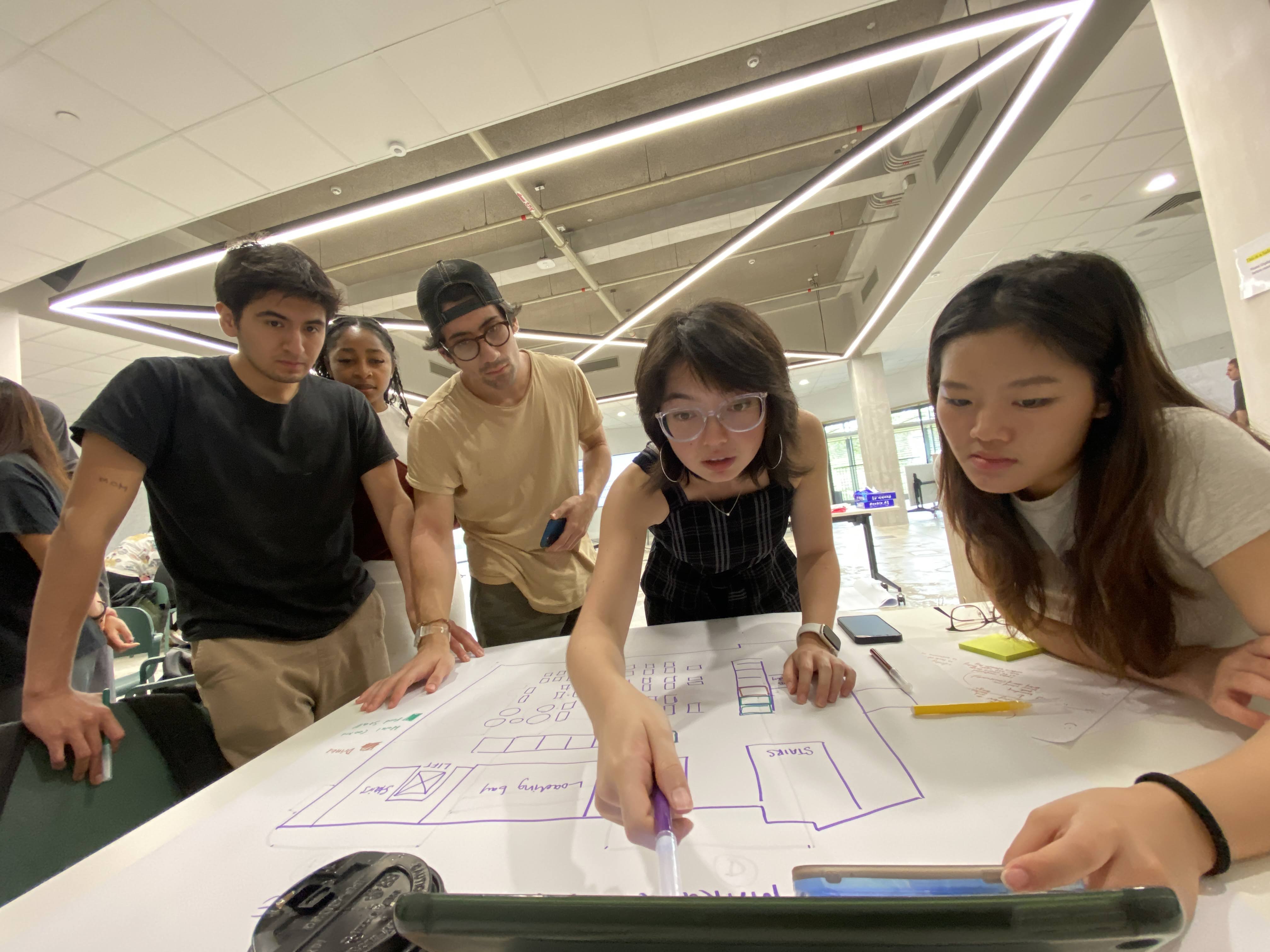 A group of four students examine a blueprint.
