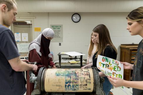 A group of students using a letterpress machine to print posters