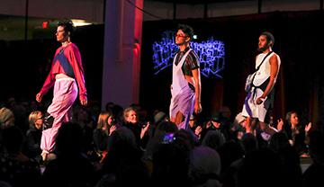 Three models walk runway at fashion show.