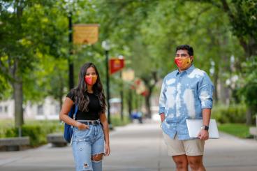 Two students walking on campus together wearing masks